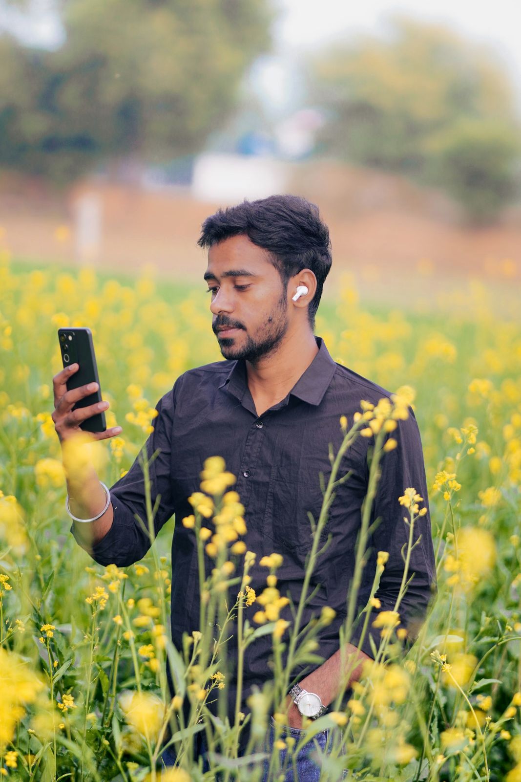 Young farmer with earphones using his smartphone in a mustard field